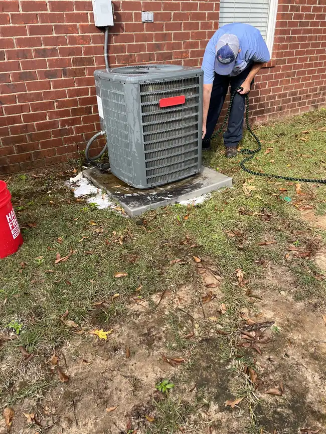 A technician working on an outdoor air conditioning unit providing heating and cooling services in Spanish Fort