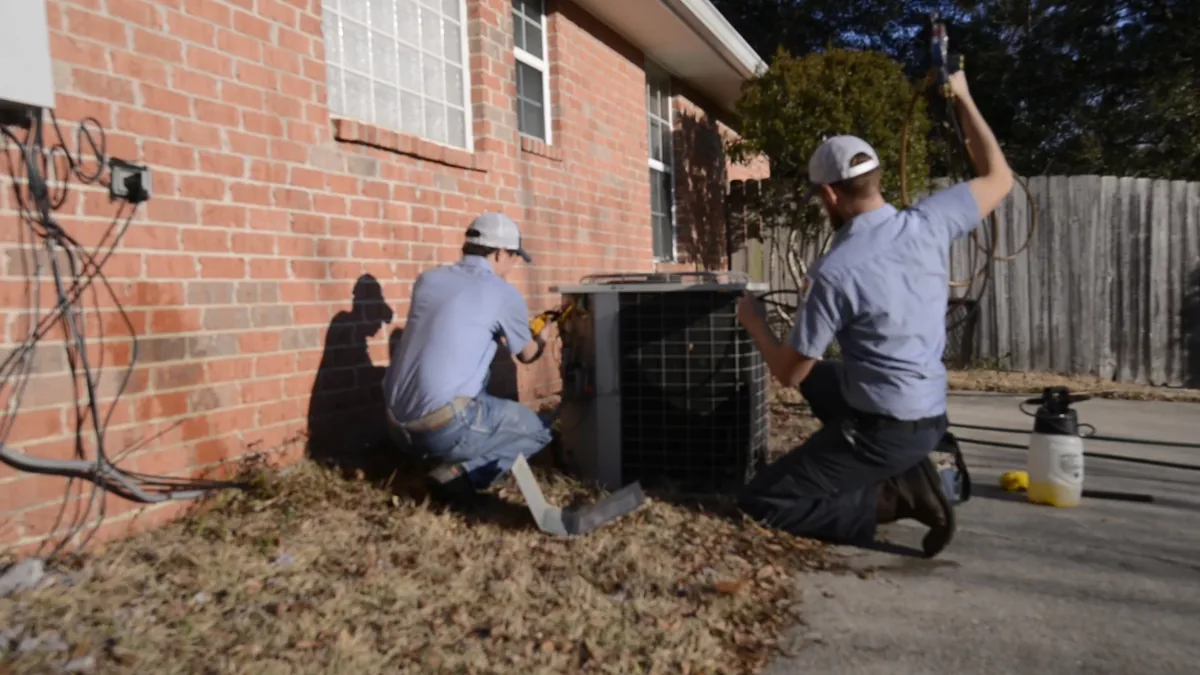 Two Climate Masters technicians working together on an outdoor condensing unit beside a Spanish Fort home.