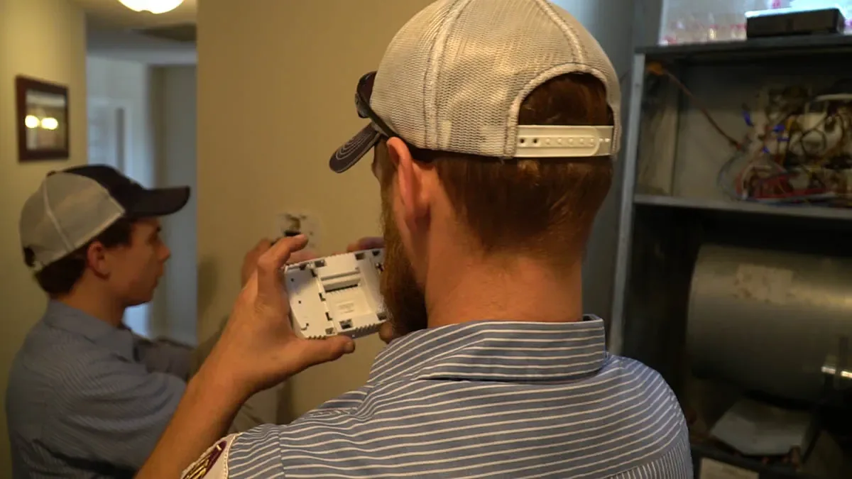 Two technicians wiring a smart thermostat installation