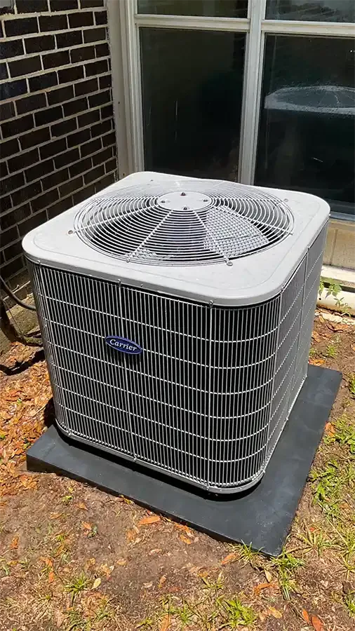 A newly installed Carrier outdoor condensing unit standing on a fresh composite pad against the brick wall of a home