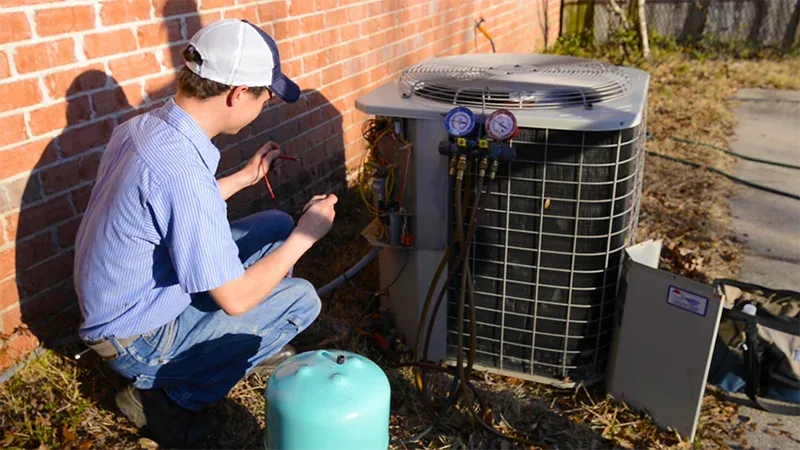 A Climate Masters technician checking an outdoor air conditioning unit with refrigerant gauges during a preventative AC maintenance visit