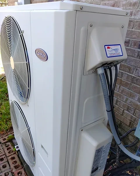 Carrier outdoor mini-split condensing unit installed beside a brick wall with Climate Masters service sticker