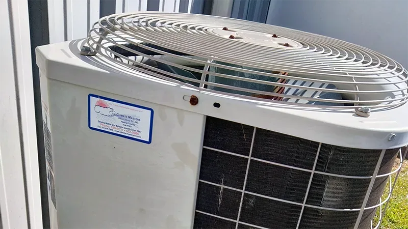 Close-up of an outdoor condenser fan grille with a Climate Masters, Inc. service sticker on the cabinet
