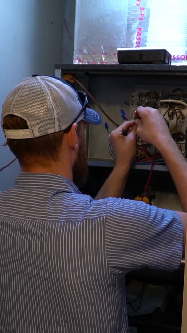 Climate Masters, Inc. technician evaluating an indoor air handler and heating unit with a multimeter