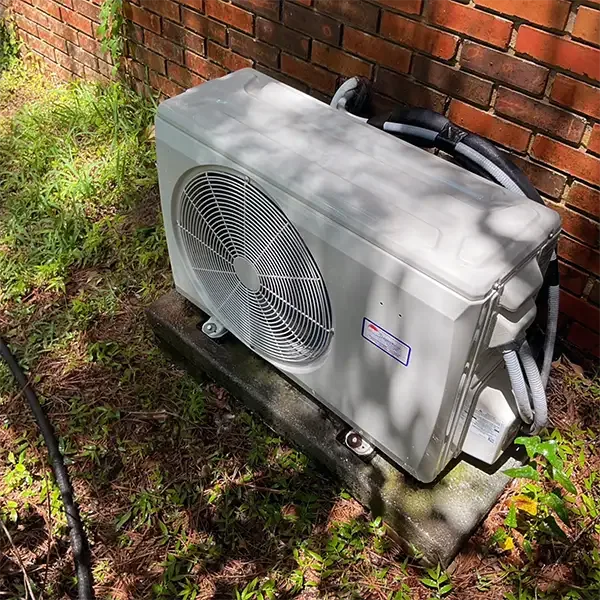 A ductless mini-split outdoor condenser mounted on a concrete pad against a brick wall