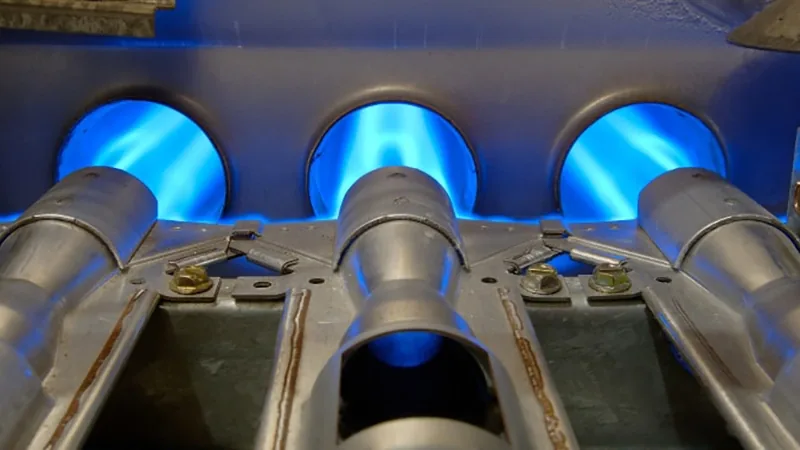 Three clean natural gas burners lit blue inside a furnace cabinet in Bay Minette