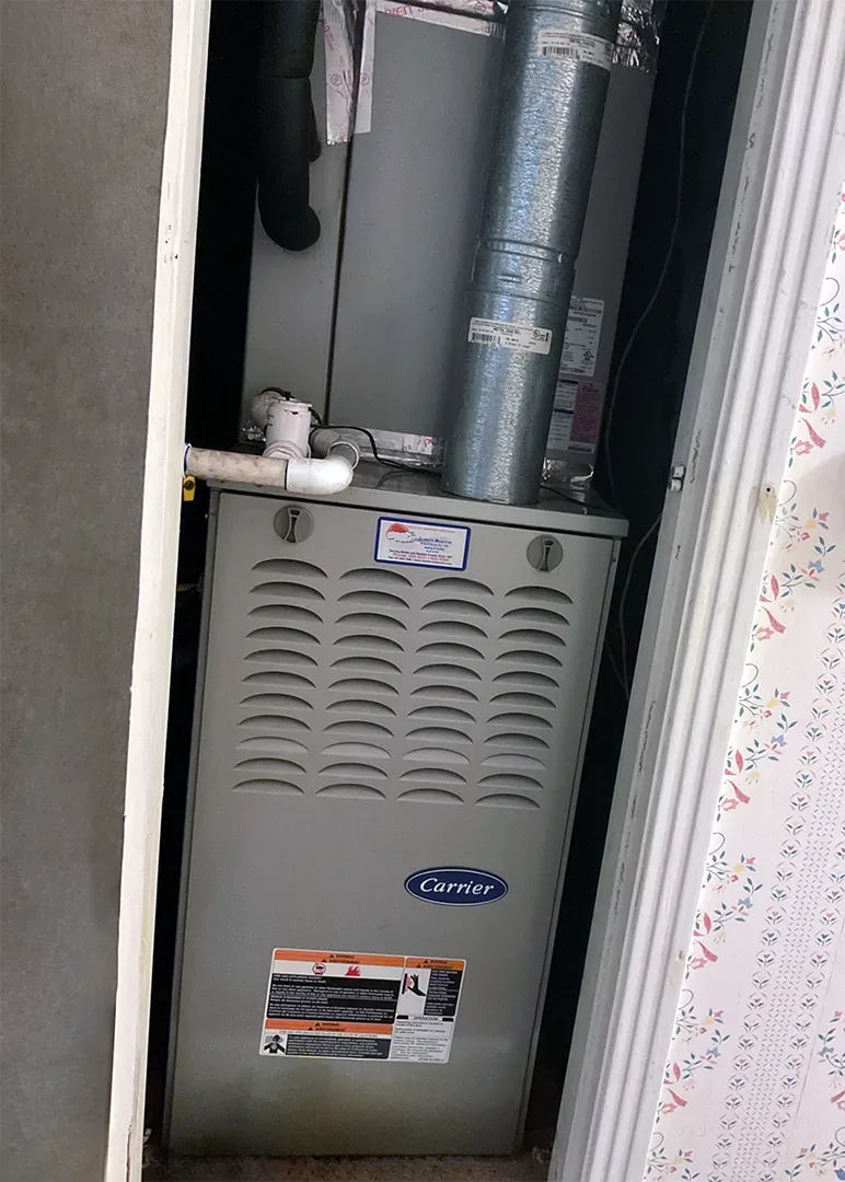 A grey Carrier furnace installed in a closet with flexible ductwork running above it