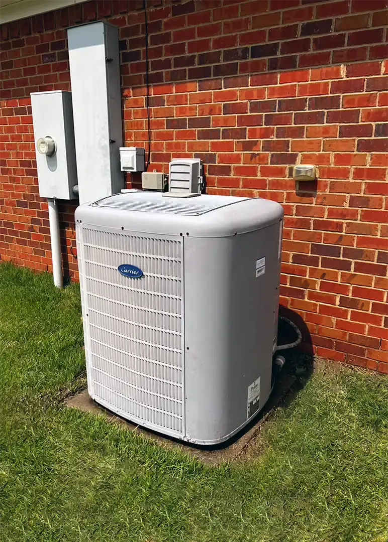 A new Carrier heat pump condensing unit installed by a red brick wall in Spanish Fort below the electrical disconnect