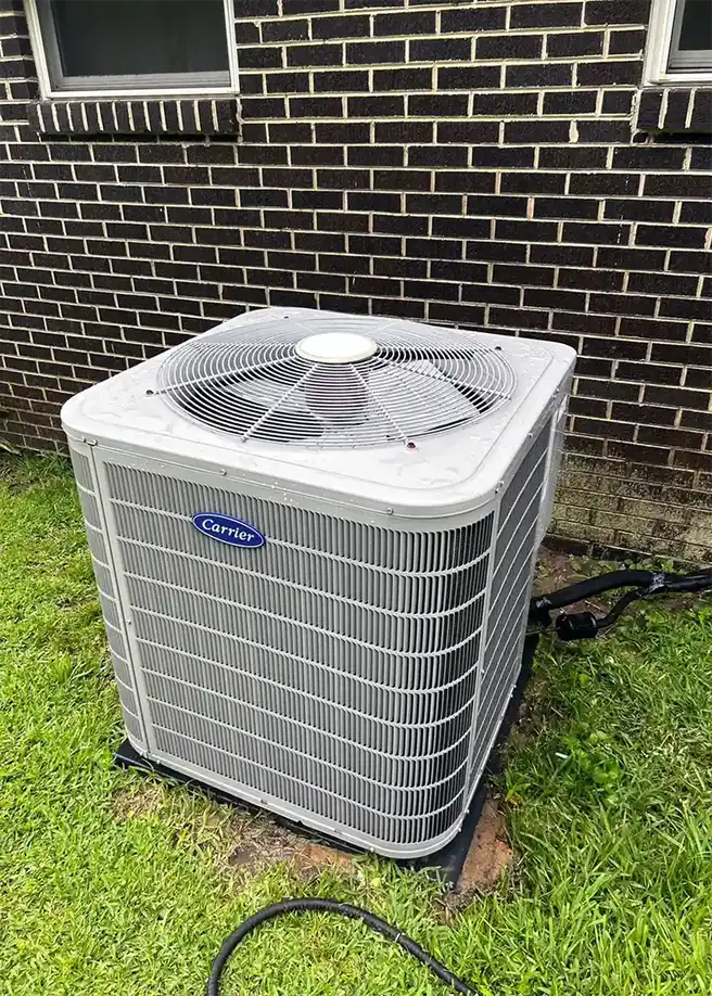 A newly installed Carrier condensing unit on a pad beside a brick house