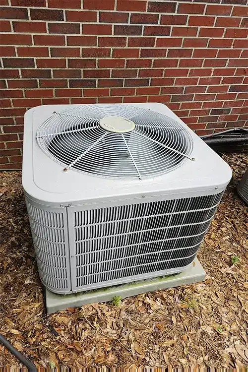 A newly installed heat pump condenser on its pad against a red brick wall