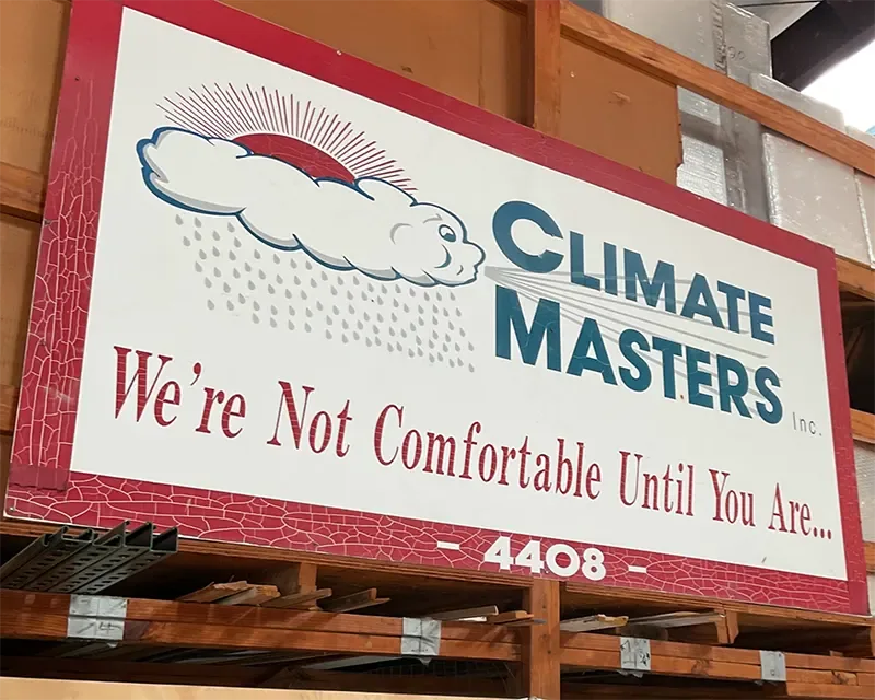 The Climate Masters sign reading 'We're Not Comfortable Until You Are' resting on a warehouse rack in Spanish Fort