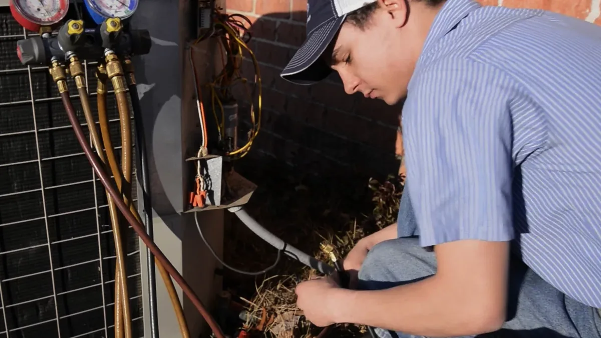 Technician working at an outdoor heat pump unit with refrigerant gauges