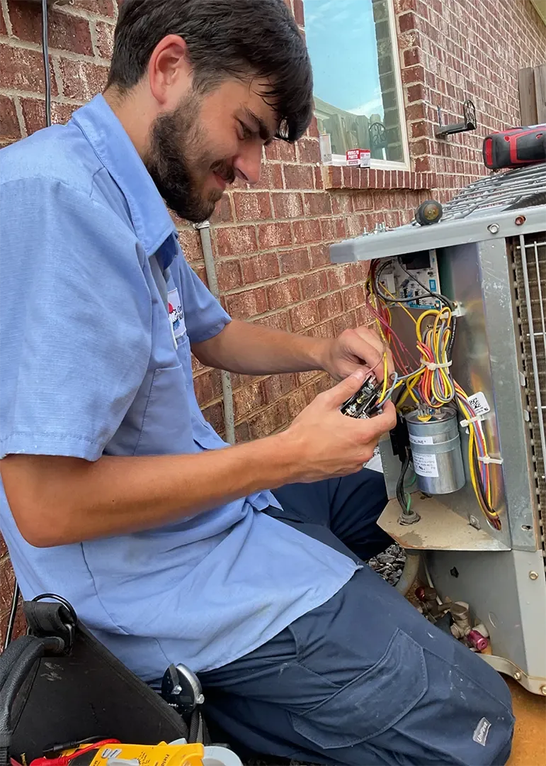 A Climate Masters technician kneeling beside an opened outdoor condenser, working on its wiring