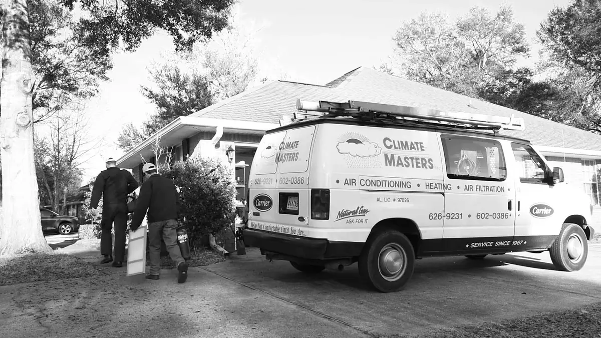 Two Climate Masters, Inc. technicians carrying equipment toward a house past their branded service van